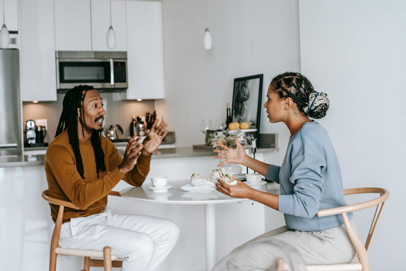 Side view of young African American male with dreadlocks in casual outfit having argument with African American dissatisfied female