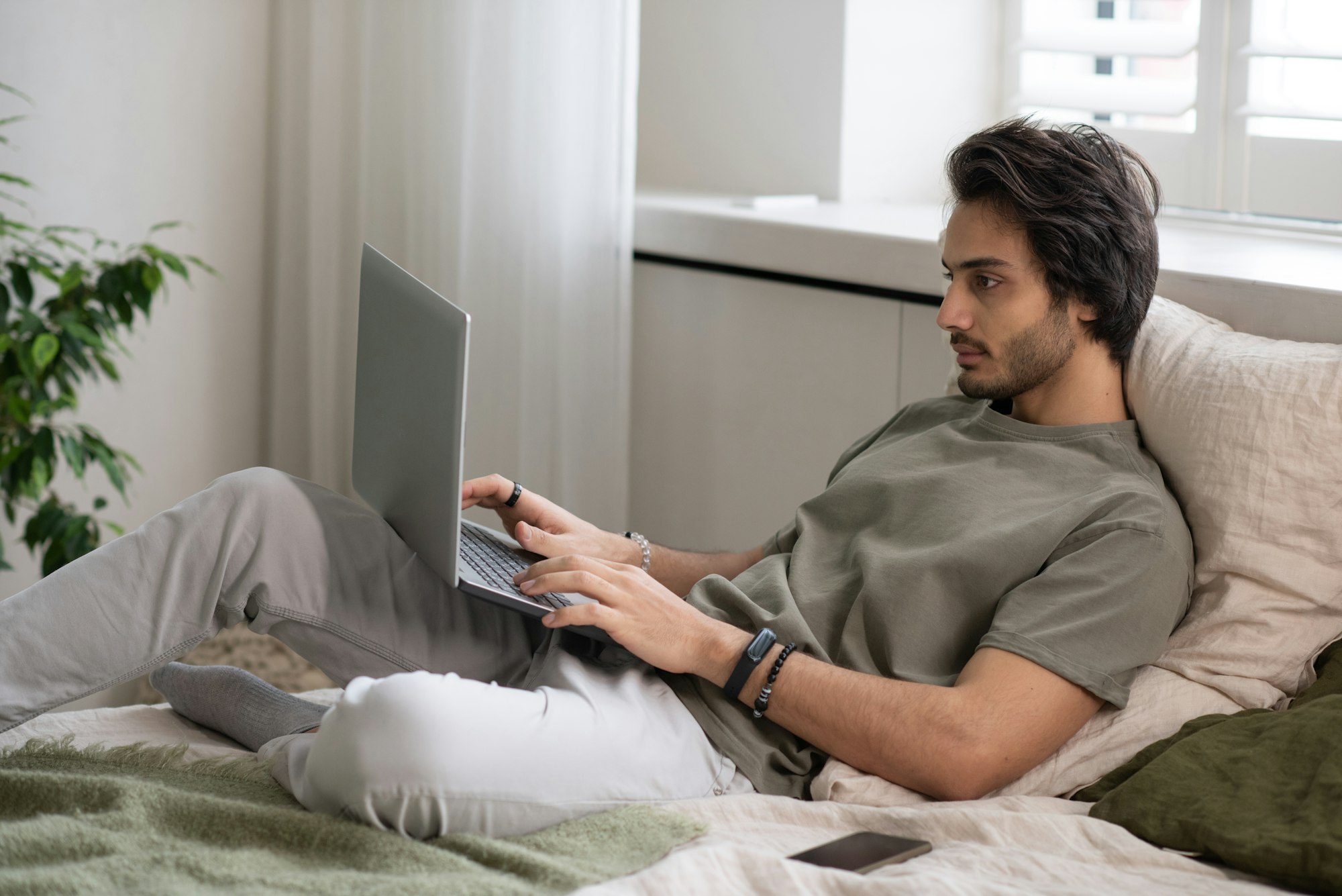 Young businessman in casualwear lying on bed and typing on laptop keyboard