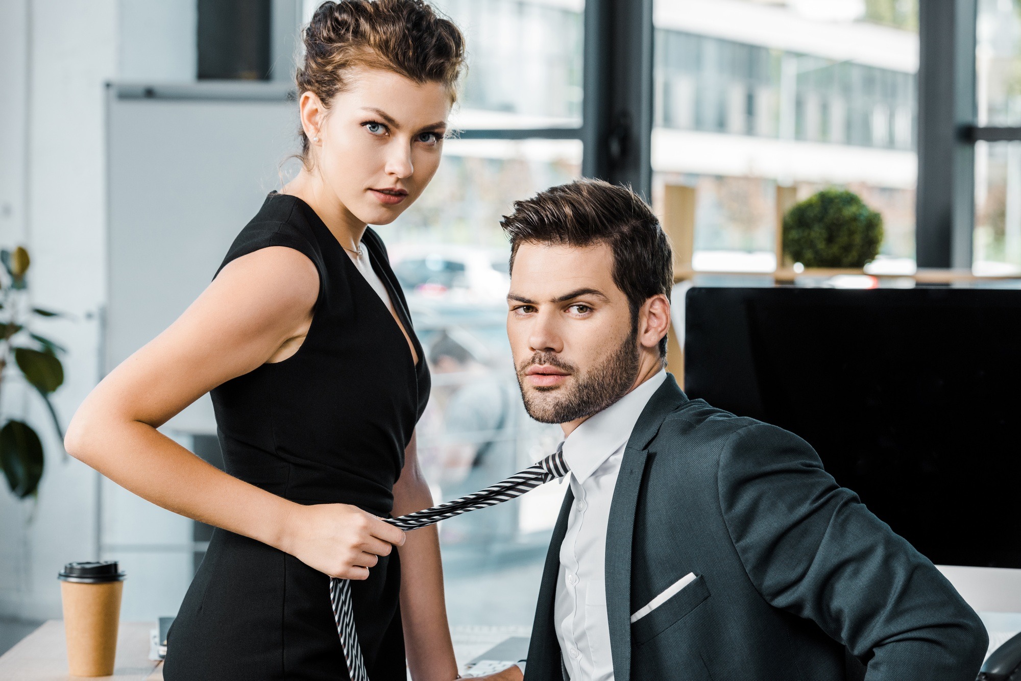 side view of businesswoman holding colleagues tie while flirting at workplace in office